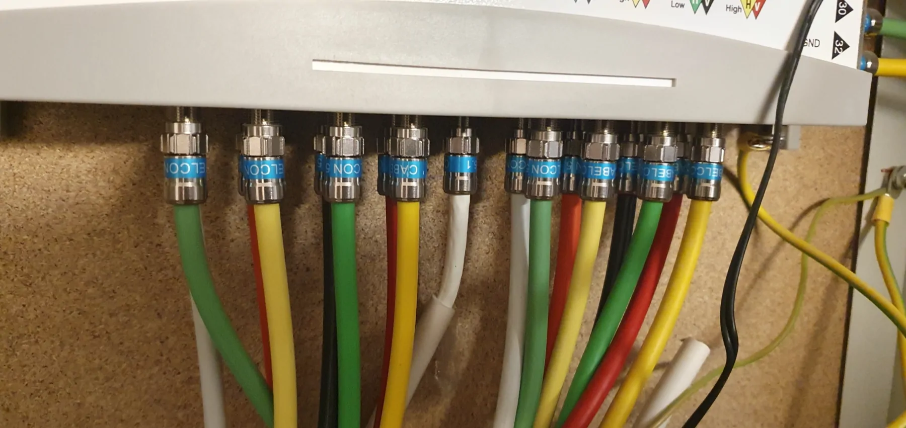 Connecteurs métalliques et câbles coaxiaux de plusieurs couleurs sous un équipement TV.