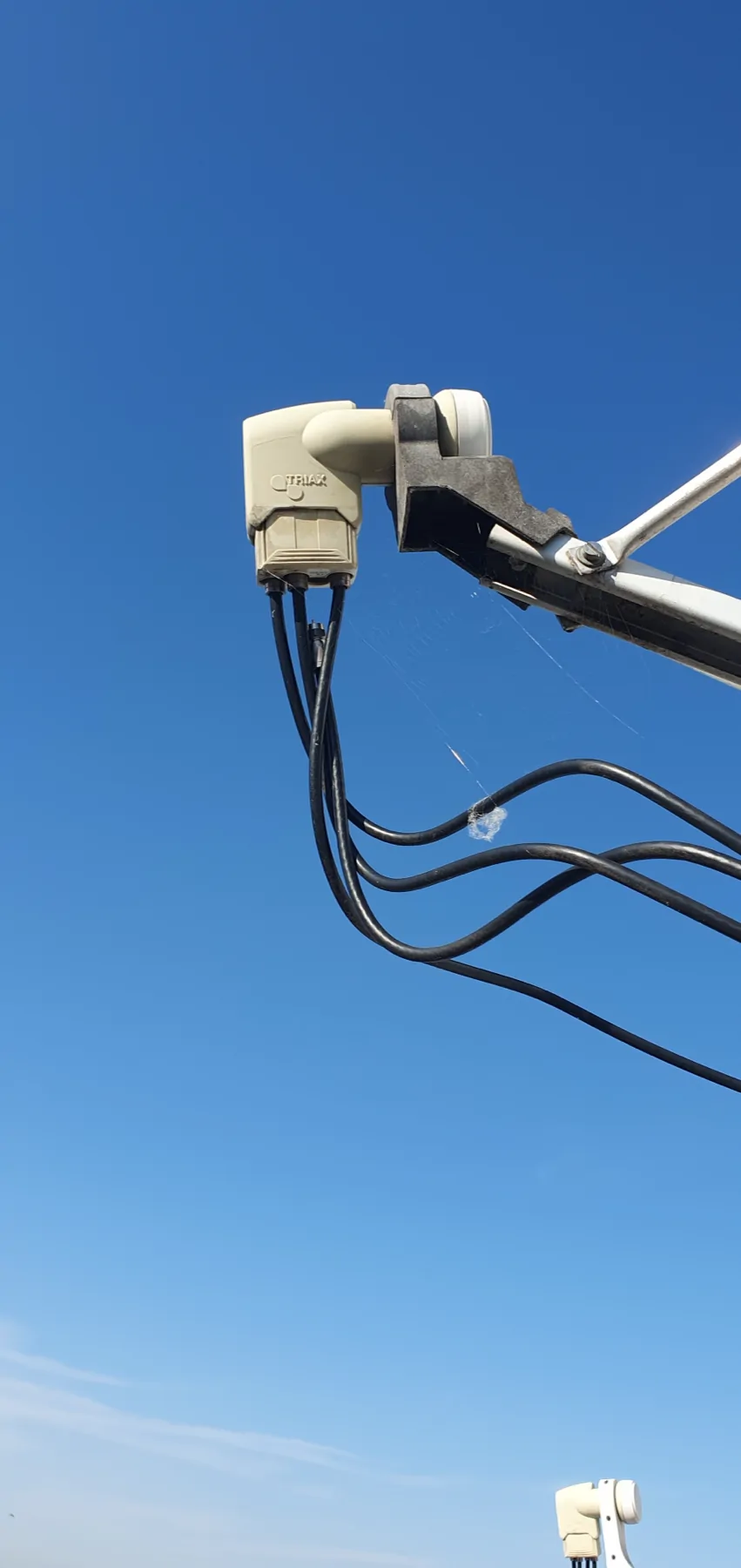 Tête de réception d’une parabole et câbles coaxiaux photographiés devant le ciel.