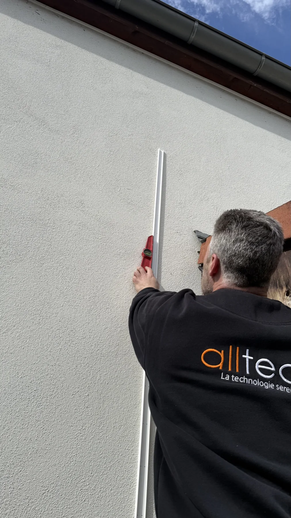 Technicien Alltech de dos plaçant un niveau contre une goulotte sur une façade.