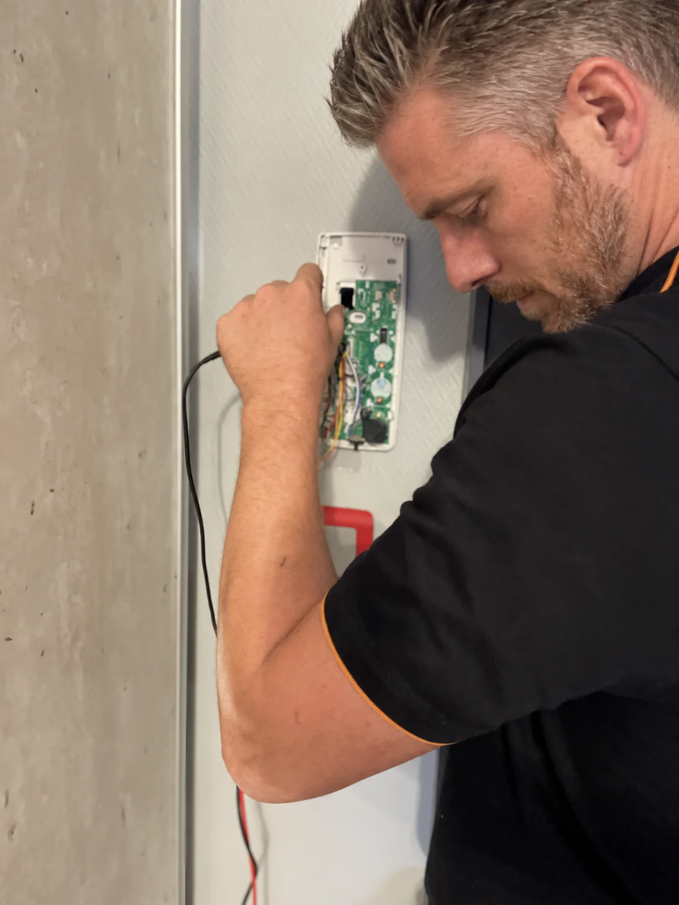 Technicien Alltech de profil travaillant sur un combiné mural ouvert.