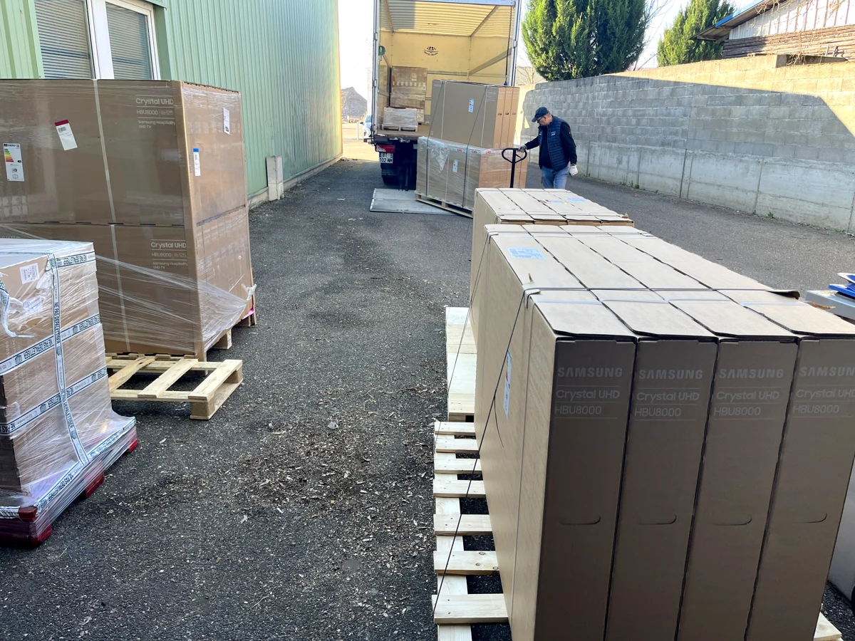 Plusieurs palettes de téléviseurs près d’un camion avec un intervenant au transpalette.