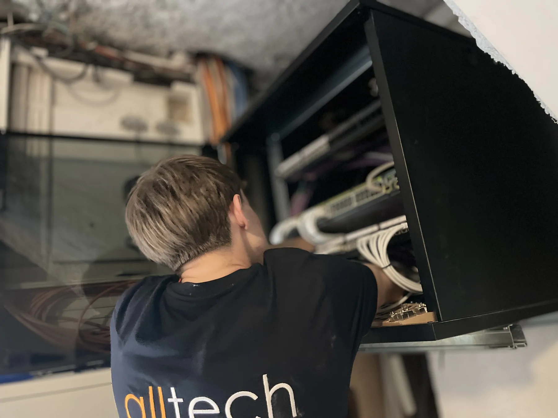 Intervenant Alltech de dos devant une baie de brassage murale ouverte.
