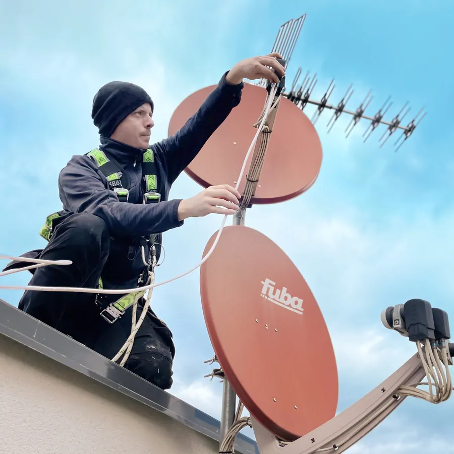 Antenniste Alltech sécurisé par harnais réglant antenne et paraboles sur un toit